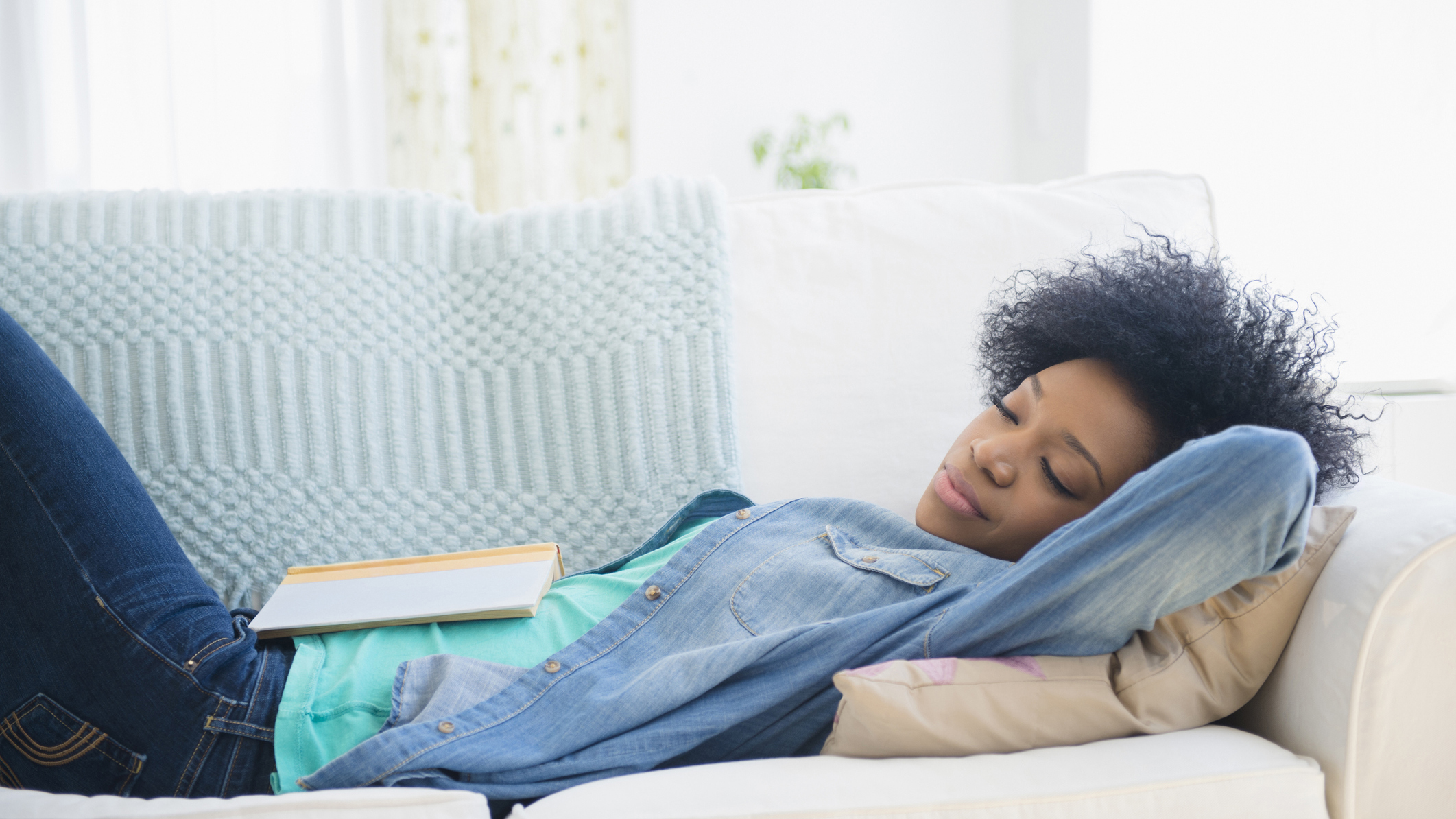 A woman wearing a denim shirt naps on her couch