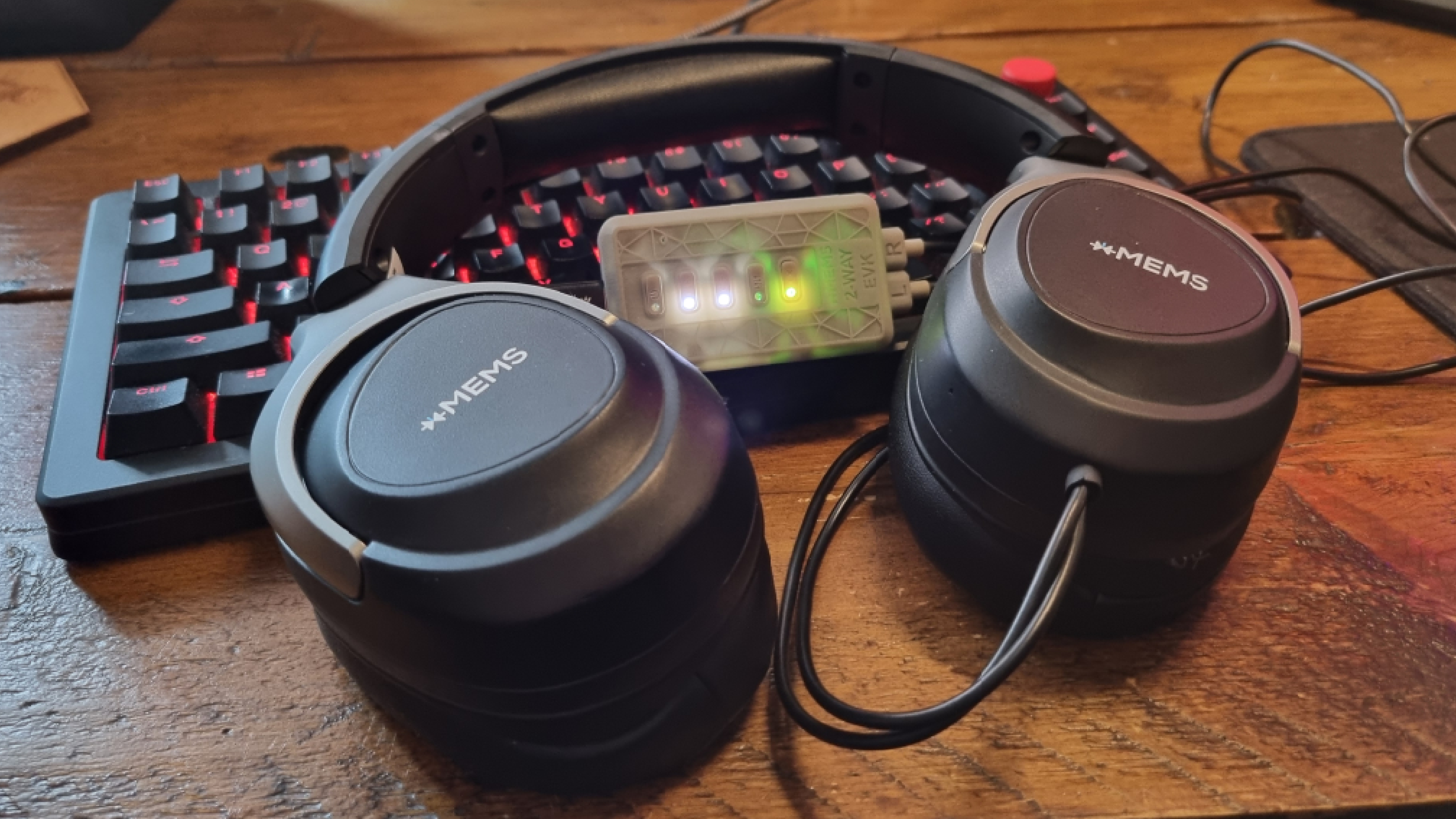 An xMEMS prototype gaming headset on a gaming keyboard lit up in red, with the control box glowing inbetween