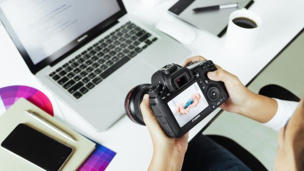 Bästa gratis bildredigeringsprogram: En person som sitter med en Canon-kamera över en laptop på ett arbetsskrivbord.