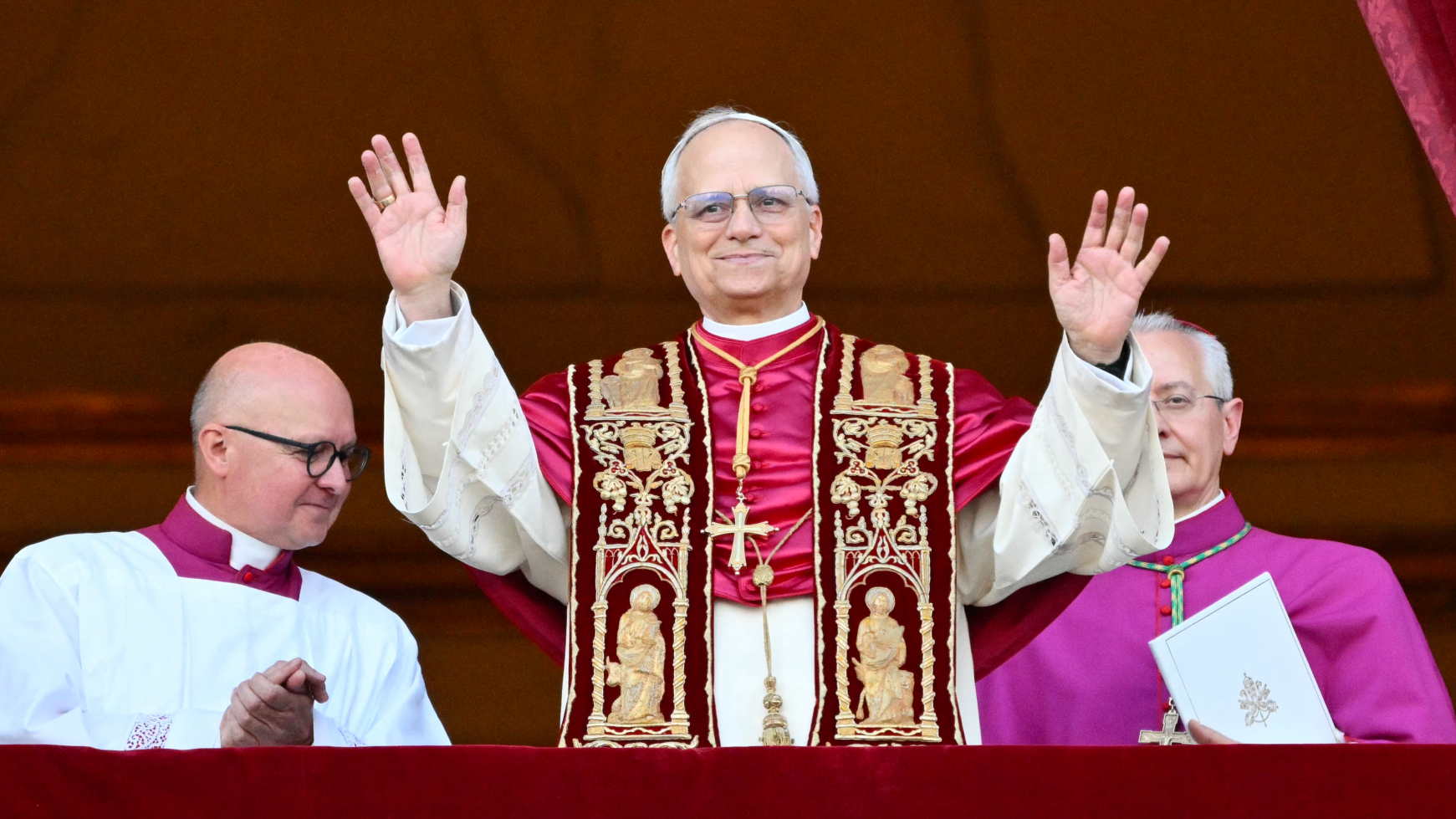 Pope Leo XIV stands in papal robes in the middle of two other men on the Vatican loggia