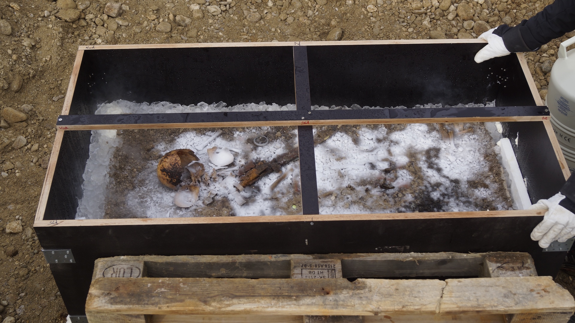 a frozen grave with a skeleton in it is carried in a box by an archaeologist