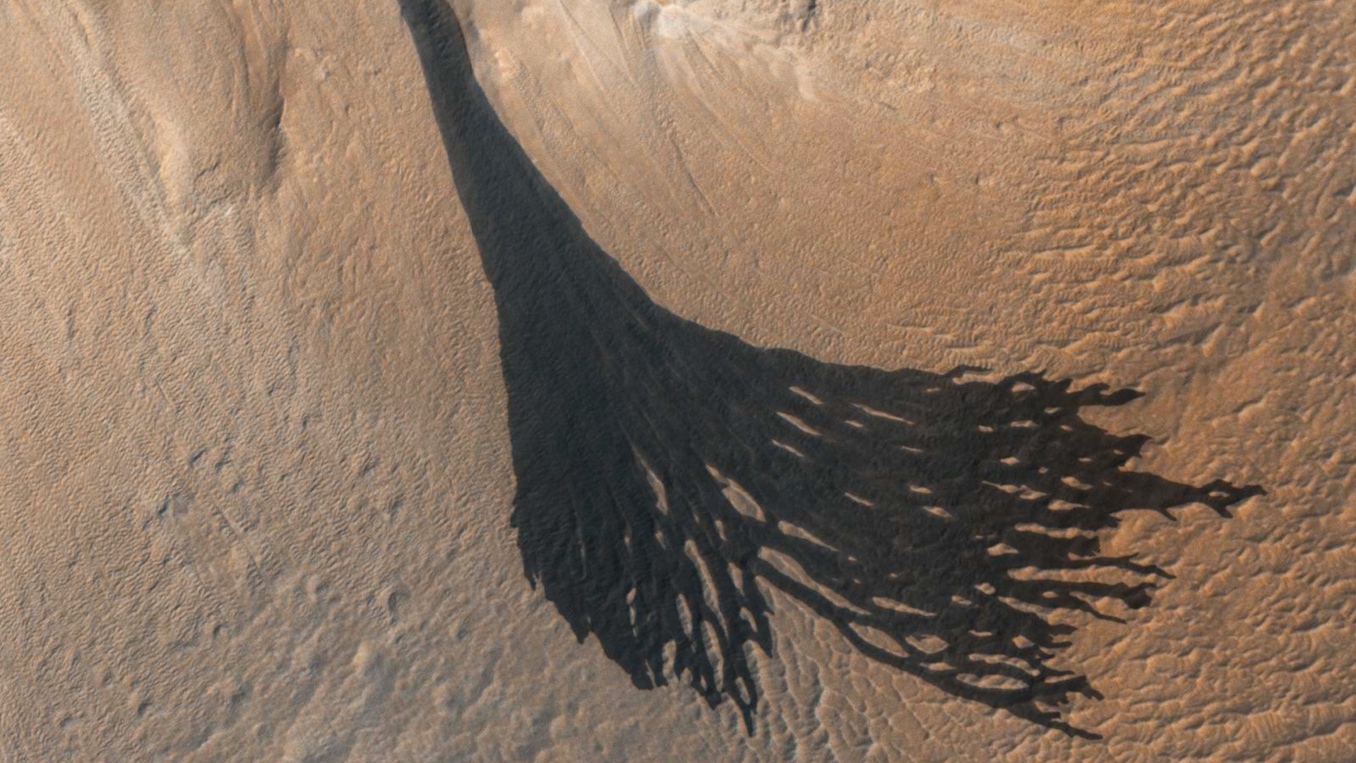 An aerial image of the surface of Mars showing dark streaks across the terrain